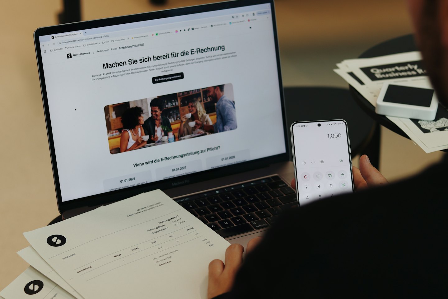 Manos sostienen un smartphone con una calculadora junto a informes de negocios.